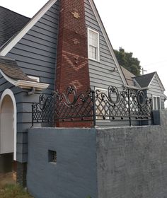 a grey house with a red brick chimney and black wrought iron fence on the front