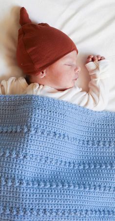 a baby sleeping on top of a bed wearing a blue blanket and a red hat