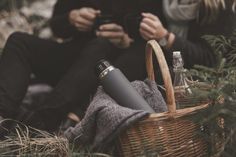 two people sitting next to each other near a basket with bottles in it and one person holding a cell phone