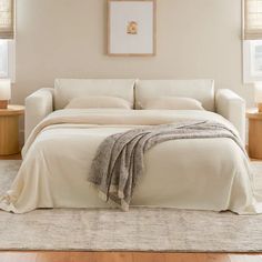 a white bed sitting in a bedroom on top of a wooden floor next to two windows