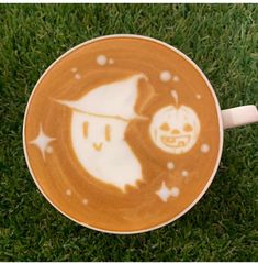 a coffee cup with a drawing of a pumpkin and a ghost on it sitting in the grass