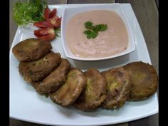 a white plate topped with fried food next to a bowl of dip and tomatoes on the side