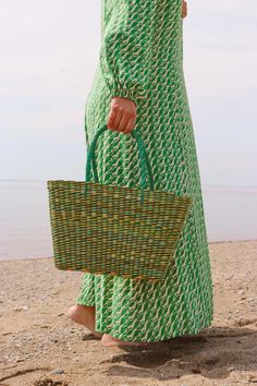 a woman carrying a green and white basket on the beach