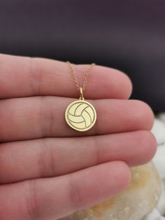 a hand holding a gold necklace with a volleyball ball on it