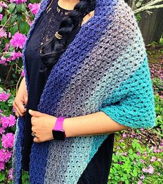 a woman wearing a multicolored crocheted shawl in front of flowers