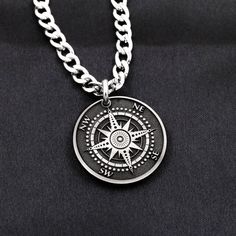 a silver necklace with a compass charm on it's link and a black background