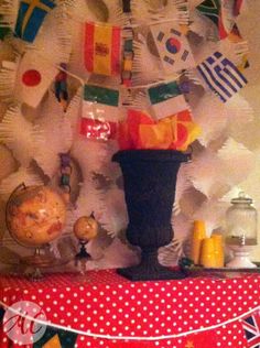 a table topped with a black vase filled with lots of different items next to a wall covered in flags