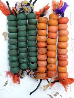 an assortment of different colored beads hanging on a white wall with orange and green feathers