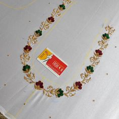 a white table cloth with gold trimming and red flowers on it, next to a card