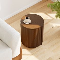 a coffee table with a cup on it next to a white chair and potted plant