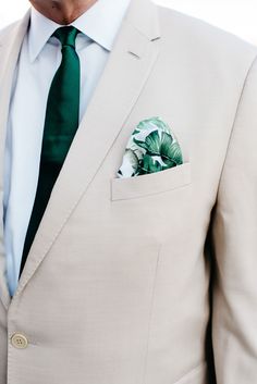 a man in a suit with a green tie and flower pocket square on his lapel