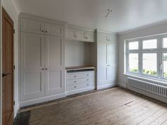 an empty room with white cupboards and drawers on the wall next to a window