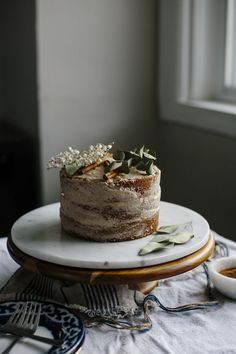 a cake sitting on top of a white plate next to a bowl of fruit and a window