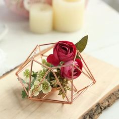 a rose in a geometric glass vase on a wooden cutting board with candles behind it