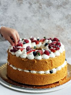 a person is decorating a cake with strawberries and blueberries on it,