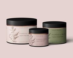 three jars of vanilla body scrubs with black lids on a pink background, one is empty and the other has a label that says vanilla