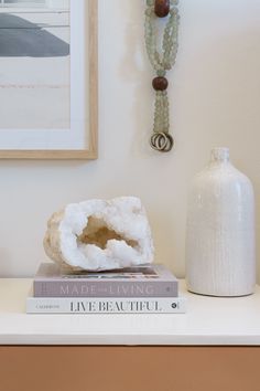 a white vase sitting on top of a table next to two books and a beaded necklace