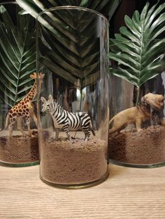 two glass vases with animals and plants in them on a table next to each other