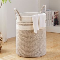 a white and beige basket sitting on top of a wooden floor next to a plant