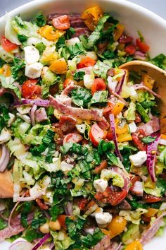 a salad with tomatoes, lettuce, onions and other vegetables in a white bowl