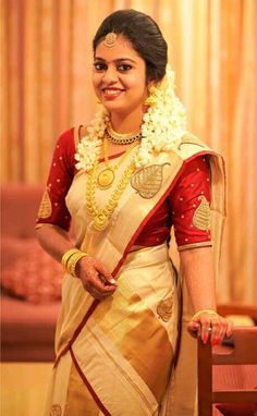 a woman in a red and white sari standing next to a wooden chair with her hands on her hips