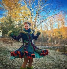 a woman in a colorful dress standing next to a tree with her arms out and smiling at the camera