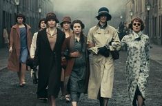 a group of women walking down a street next to each other in trench coats and hats