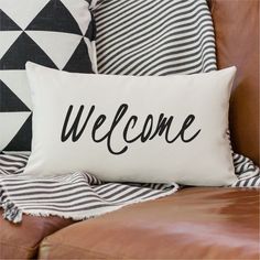 a black and white pillow with the word welcome on it sitting on a leather couch