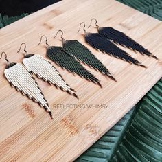 three pairs of fringe earrings sitting on top of a wooden table next to each other