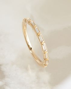 a yellow gold ring with baguettes on it sitting on a white surface,