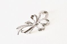 Vintage silver crosshatch clear rhinestone bow brooch. Statement flourish clear crystal sparkle Christmas silver bow four loop lapel brooch. Vintage silver tone four loop flourish bow with a crosshatch texture detail and clear rhinestones. Pretty bow with clear crystals/rhinestones giving a touch of sparkle to any occasion especially over the Christmas/holiday period or for a vintage wedding yet perfect to glam up an outfit any time of the year. In good used vintage condition. Please see images Silver Brooch With Decorative Bow For Party, Silver Bow Brooch For Wedding, Elegant Silver Brooch With Bow, Silver Bow Brooches For Formal Occasions, Silver Brooch With Bow For Formal Occasions, Formal Silver Brooch With Bow Detail, Formal Silver Brooch With Bow, Formal Silver Brooch With Ribbon, Silver Wedding Brooch With Ribbon