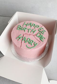 a pink birthday cake with green writing on it in a white cardboard box that says happy birthday cary