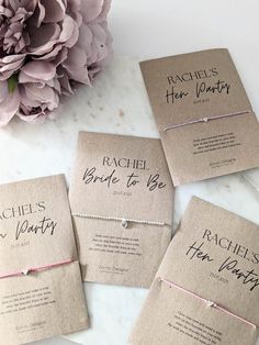 four bridesmaid bracelets with names on them sitting next to a pink flower