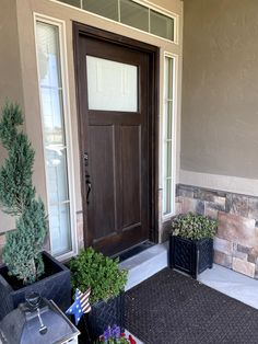 a front door with two planters on the side and an american flag rug outside