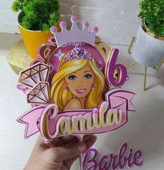 a hand holding up a cardboard cutout of a barbie doll wearing a tiara