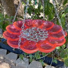 a red glass sun catcher hanging from a chain on a planter in the garden