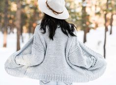 a woman wearing a white hat standing in the snow with her back to the camera