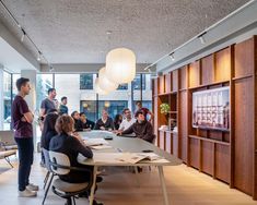 a group of people sitting around a table in a room with wooden walls and floor to ceiling windows