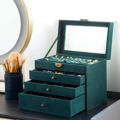 a green jewelry box sitting on top of a desk next to a mirror and pen holder