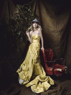 a woman in a yellow dress standing next to a red chair