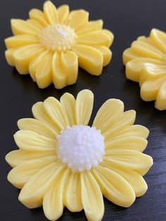 three yellow flowers sitting on top of a black table next to each other and one white flower in the middle