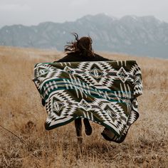 a woman walking through a field holding a blanket