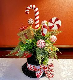 Bring the  joy of Christmas inside with this Whimsical Christmas Candies Centerpiece with  peppermint ornaments and a large gift box snuggled in a wicker top hat and greens. This arrangement will bring a touch of Christmas anywhere it is placed. Perfect for a Christmas table top, buffet or gift for someone special. Whimsical Christmas Centerpieces For Table, Candy Christmas Centerpieces, Snowman Centerpiece Ideas, Peppermint Ornaments, Christmas Center Piece, Christmas Centerpieces Cheap, Holiday Centerpieces Christmas, Christmas Table Top, Candy Centerpiece