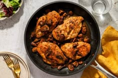 chicken and mushrooms in a skillet on a table next to plates with silverware