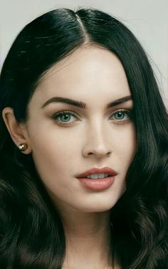 a close up of a person with long dark hair and green eyeshadow wearing gold earrings