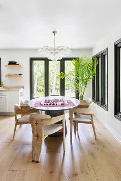 a dining room table with chairs and a potted plant in the center is surrounded by windows