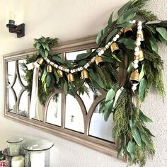 a mirror hanging on the wall with greenery and bells