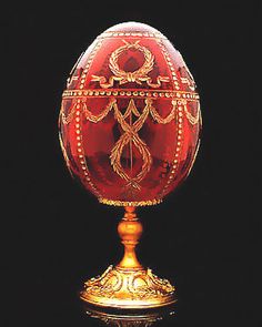 an ornately decorated red and gold egg on a black background with its reflection in the water