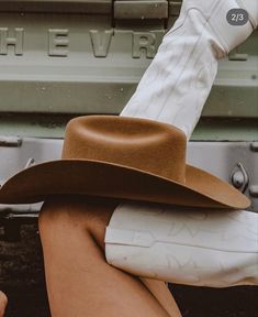 a woman sitting on the back of a truck wearing a brown hat and white boots