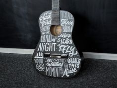 a guitar with words written on it sitting in front of a blackboard wall and floor